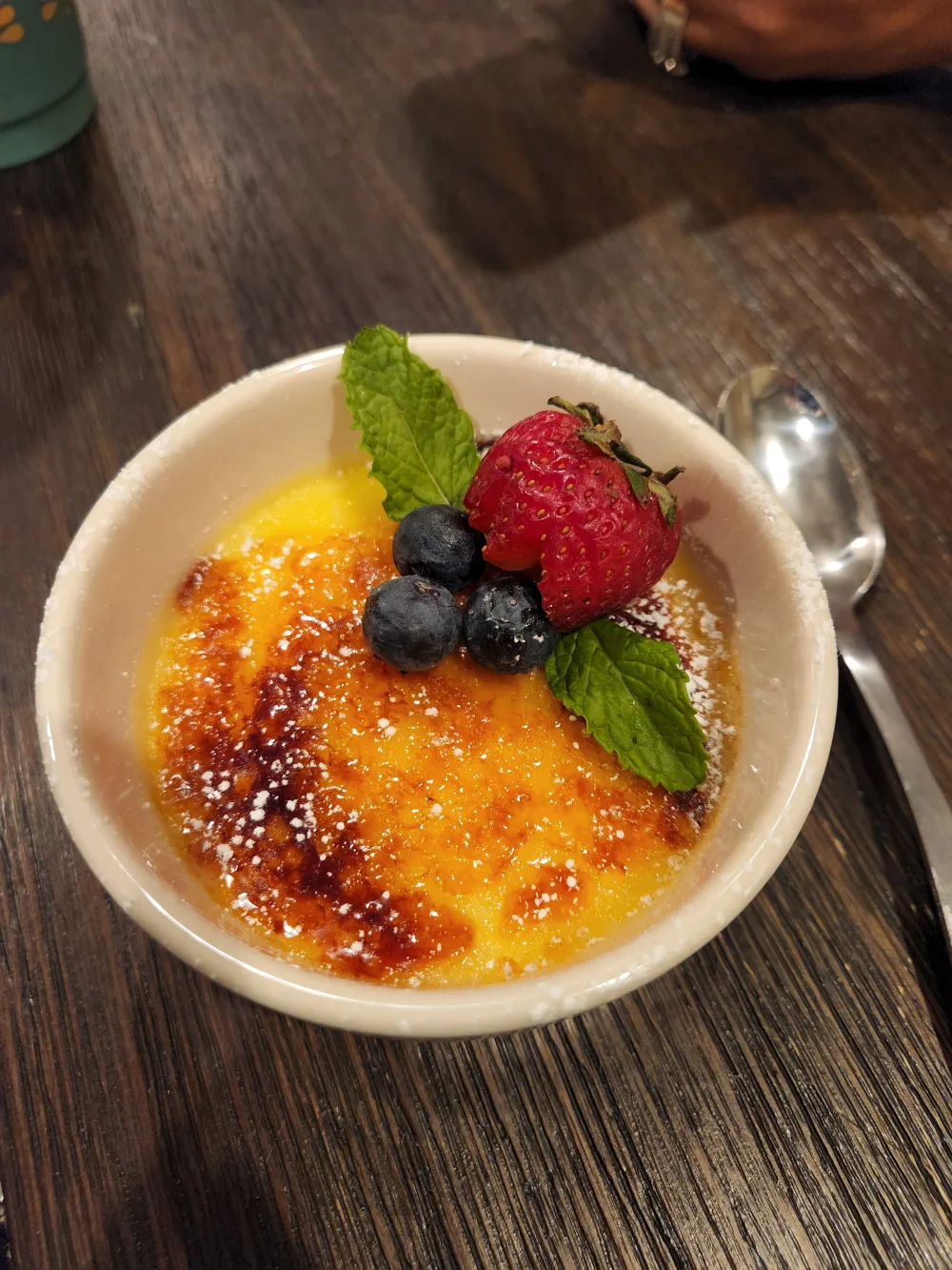 Crème brûlée in a white ramekin with a torched sugar top, dusted with powdered sugar and finished with berries and mint.