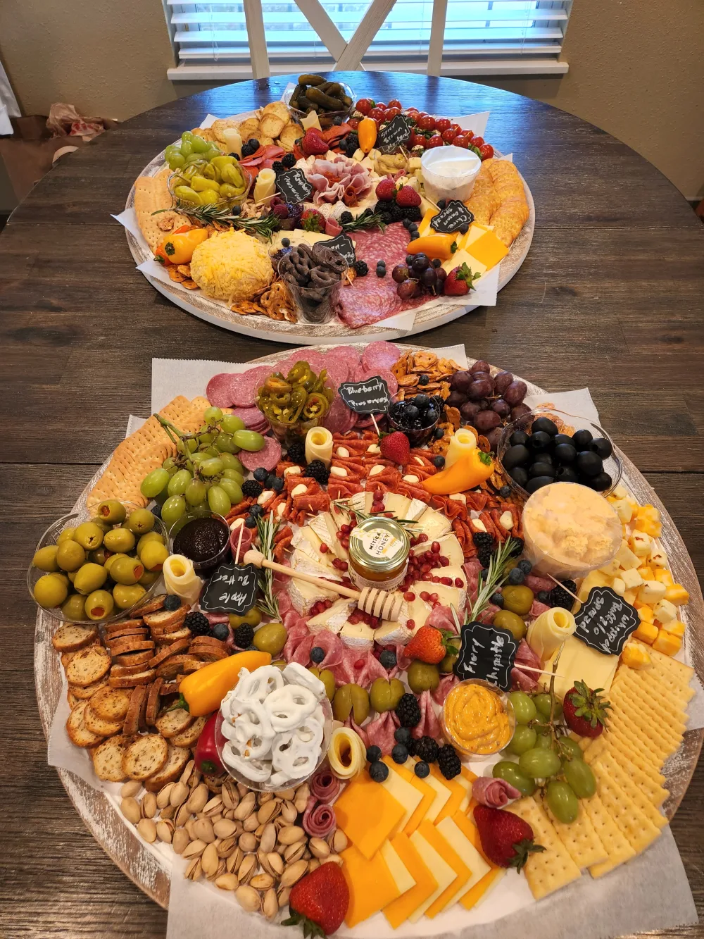 Two large event boards on a wood table: a prosciutto rose at the center, surrounded by cheeses, cured meats, fruit and crackers.