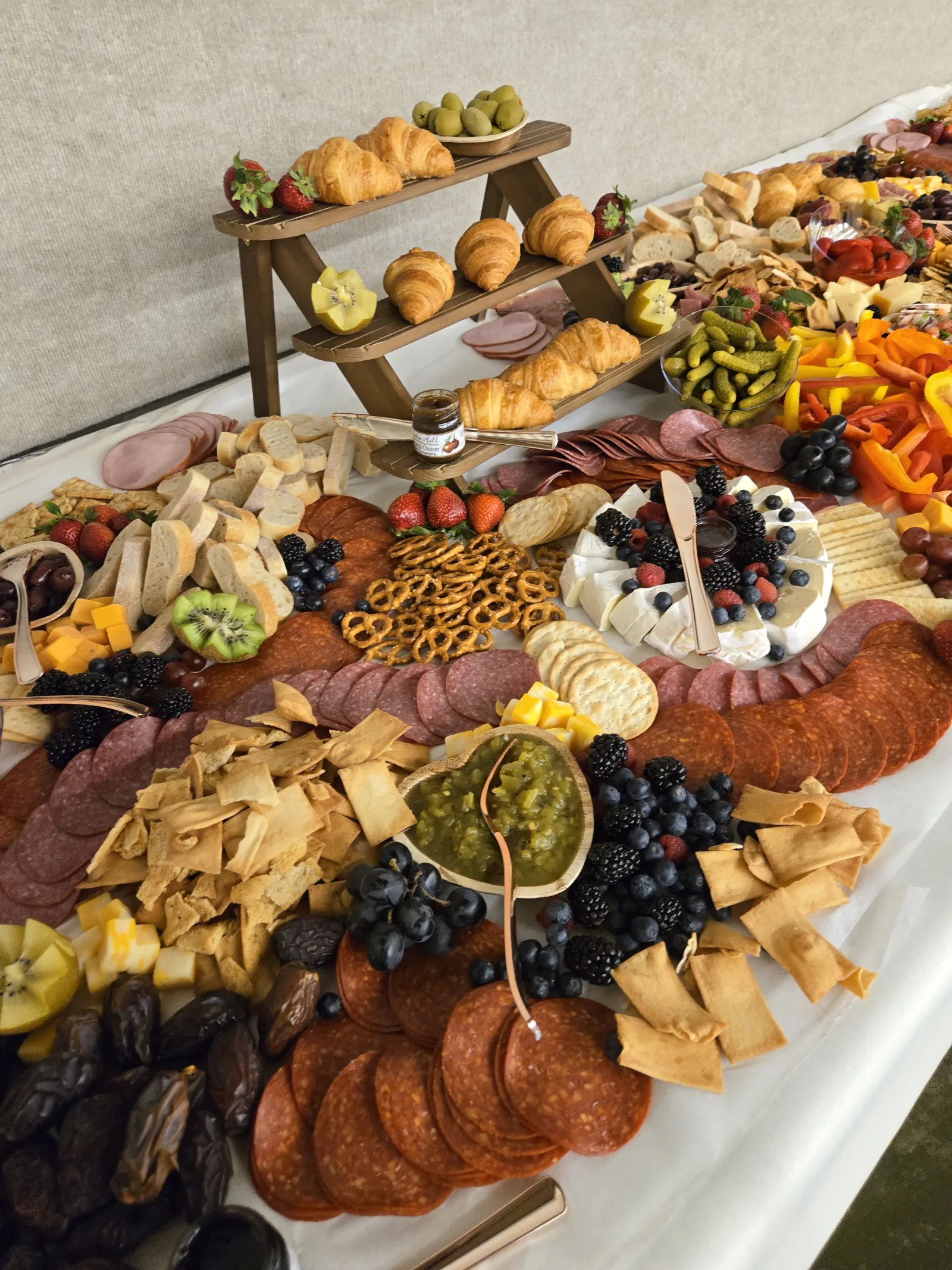 A catered spread laid along a banquet table: cured meats, croissants, cheeses, fruit and preserves, set out for a meeting.