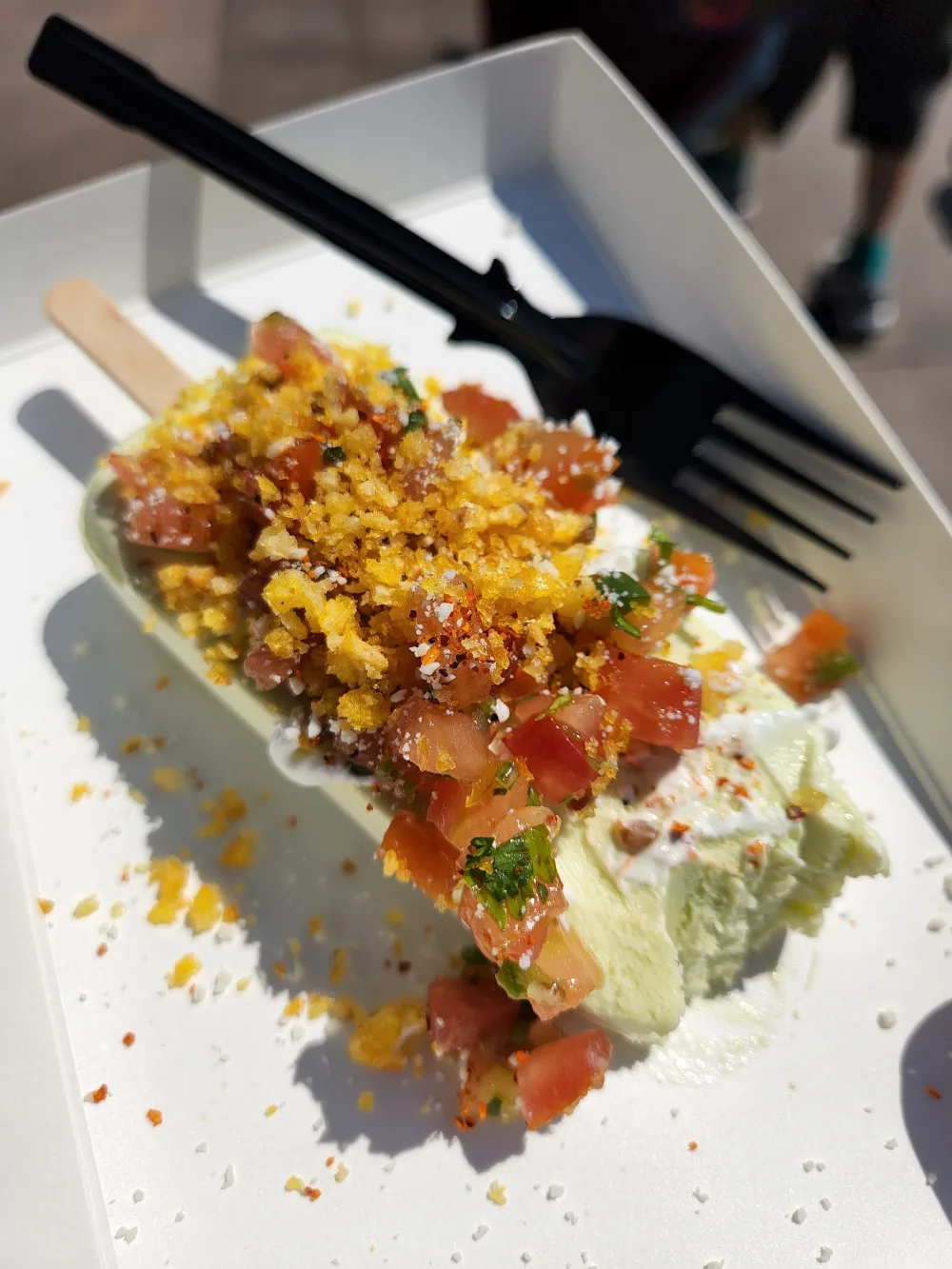 An elote paleta on a stick: avocado ice topped with pico de gallo, cotija, chile and crushed corn chips.