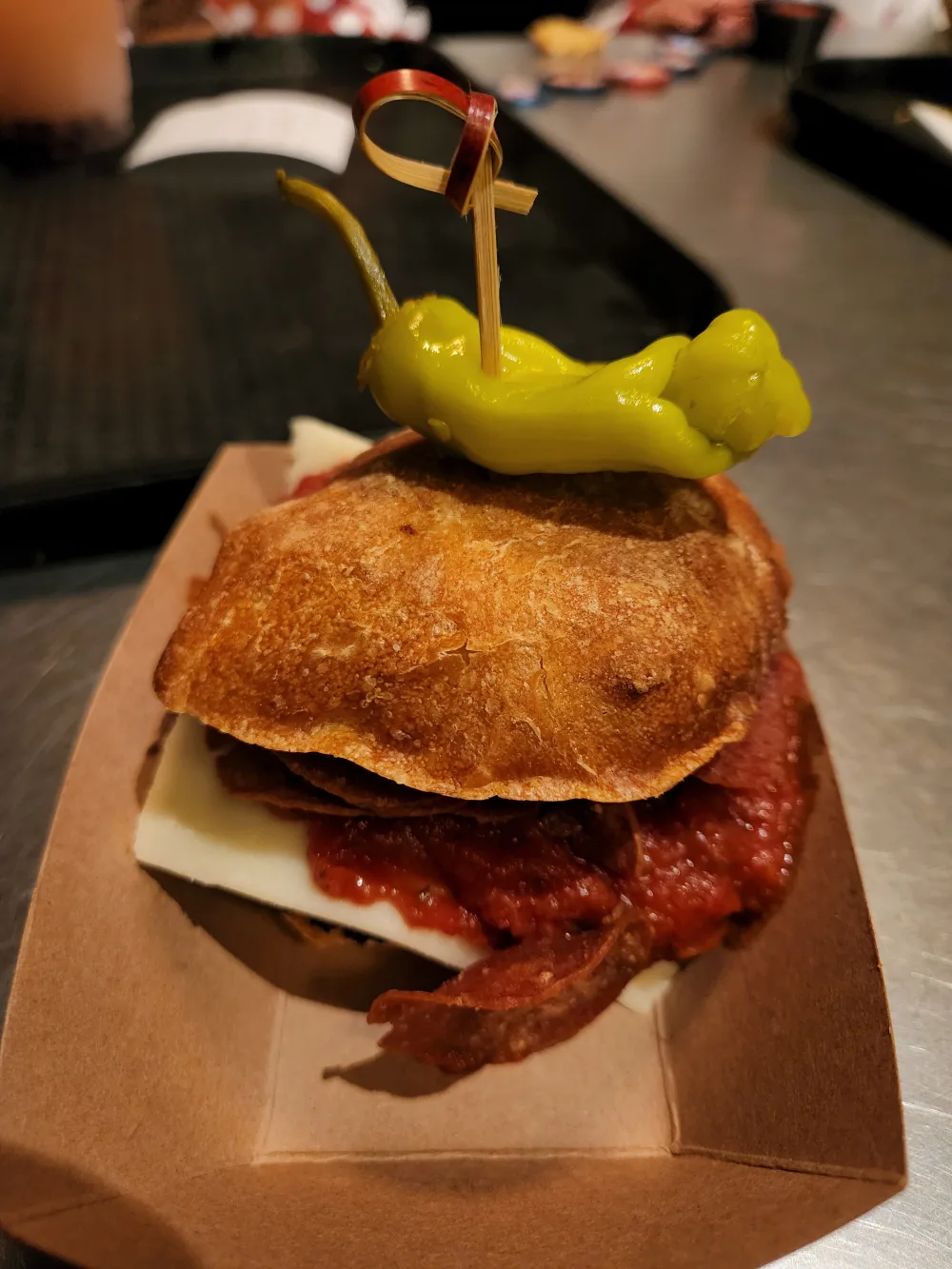 A sandwich built between crisp potato chips, layered with salami, white cheese and red sauce, pinned with a pepperoncini.
