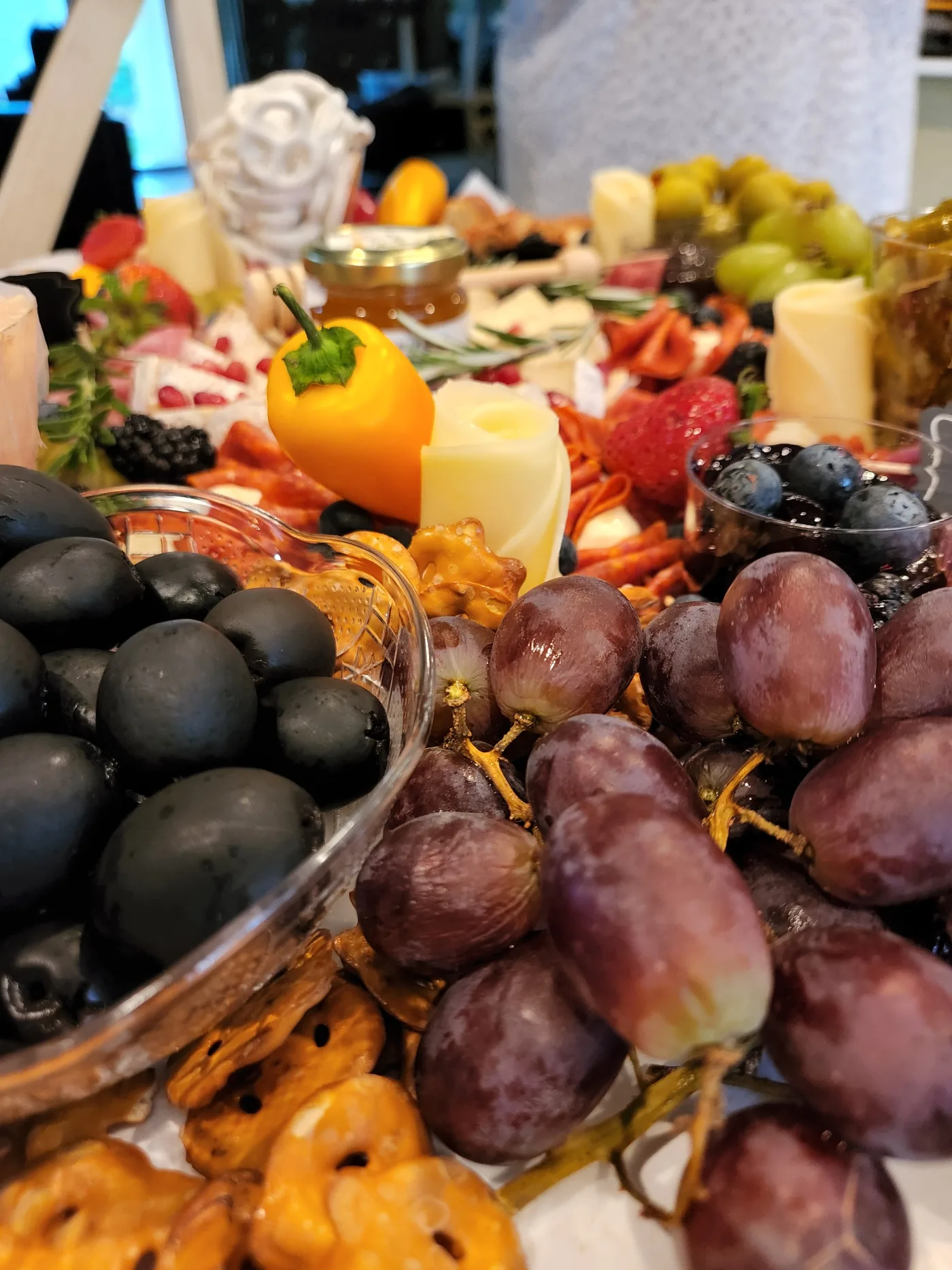 A close view of a grazing board: black olives and red grapes in the foreground, cheese and cured meats behind.