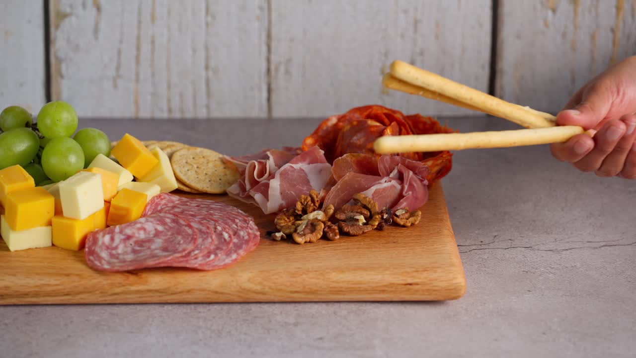 A rustic board with meats, cheeses and breadsticks.