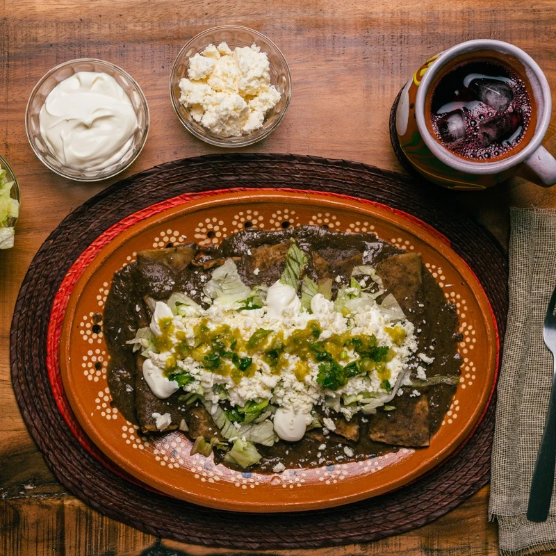 Enchiladas with green sauce and cheese on a terracotta plate.