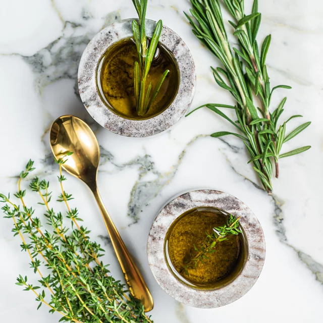 Olive oil with fresh rosemary and thyme in small stone bowls.