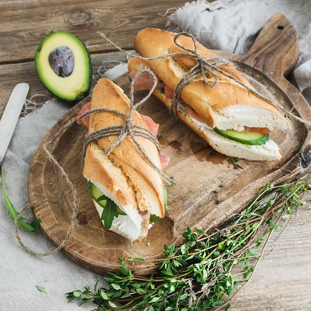 Baguette sandwiches with fresh greens on a wooden cutting board.
