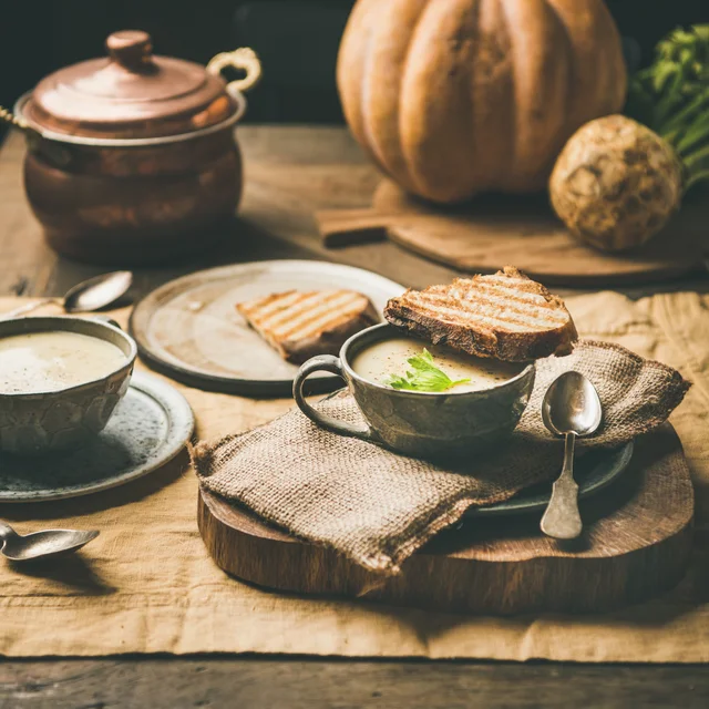 Creamy seasonal soup with toasted bread on a wooden board.