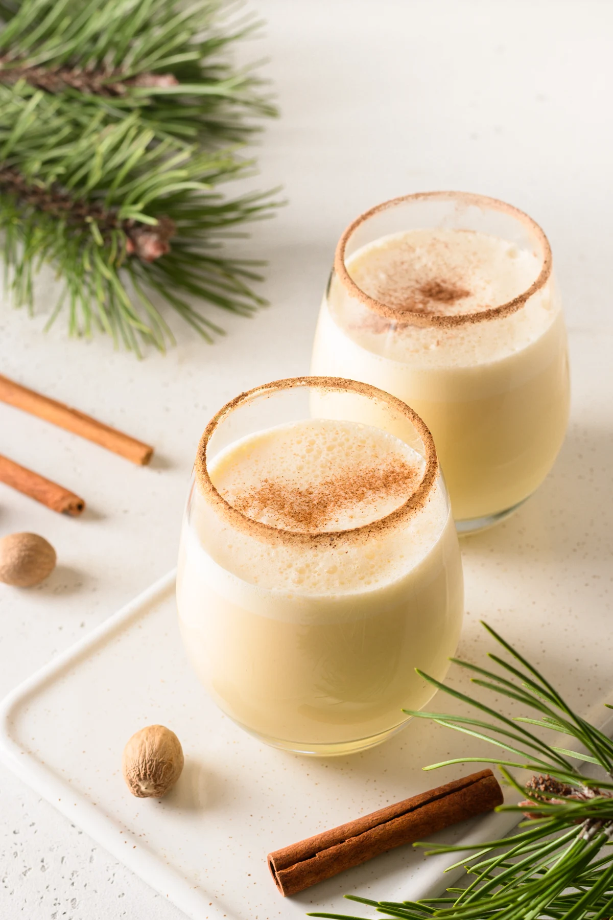 Glasses of eggnog with cinnamon and nutmeg on a light table