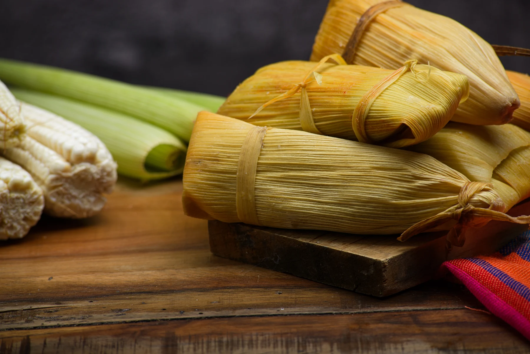 Corn-husk tamales tied by hand on a wooden board